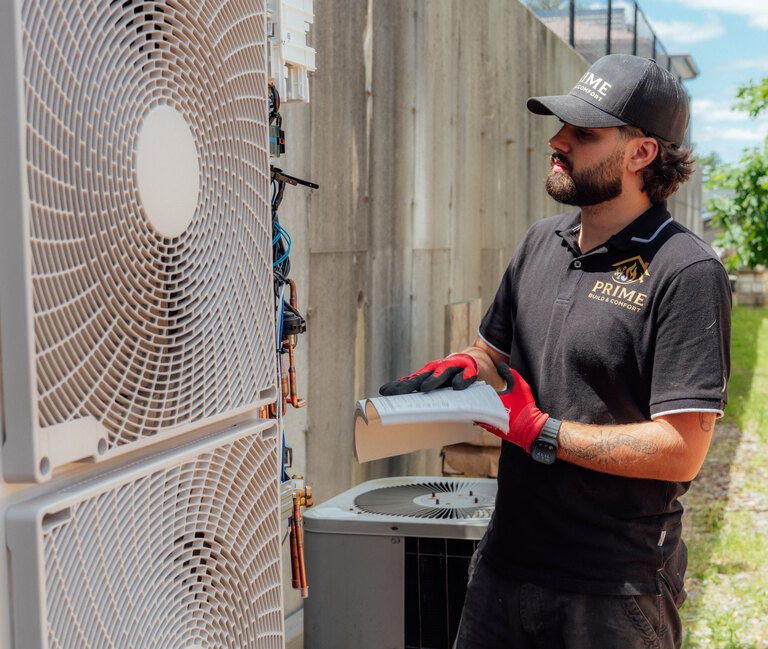 A Prime technician holding the service manual next to a newly installed outdoor condenser unit